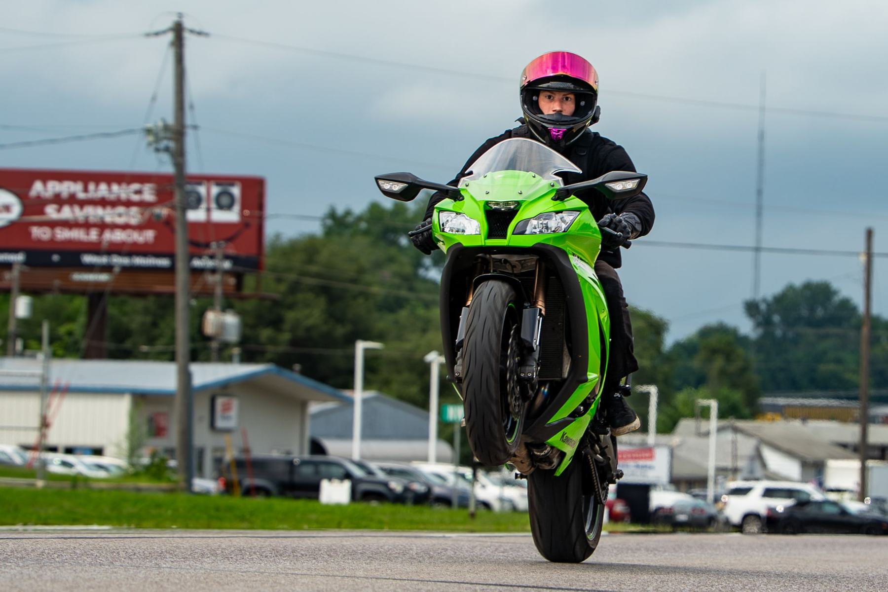 Rider on a green sport bike pulling a wheelie down an open road