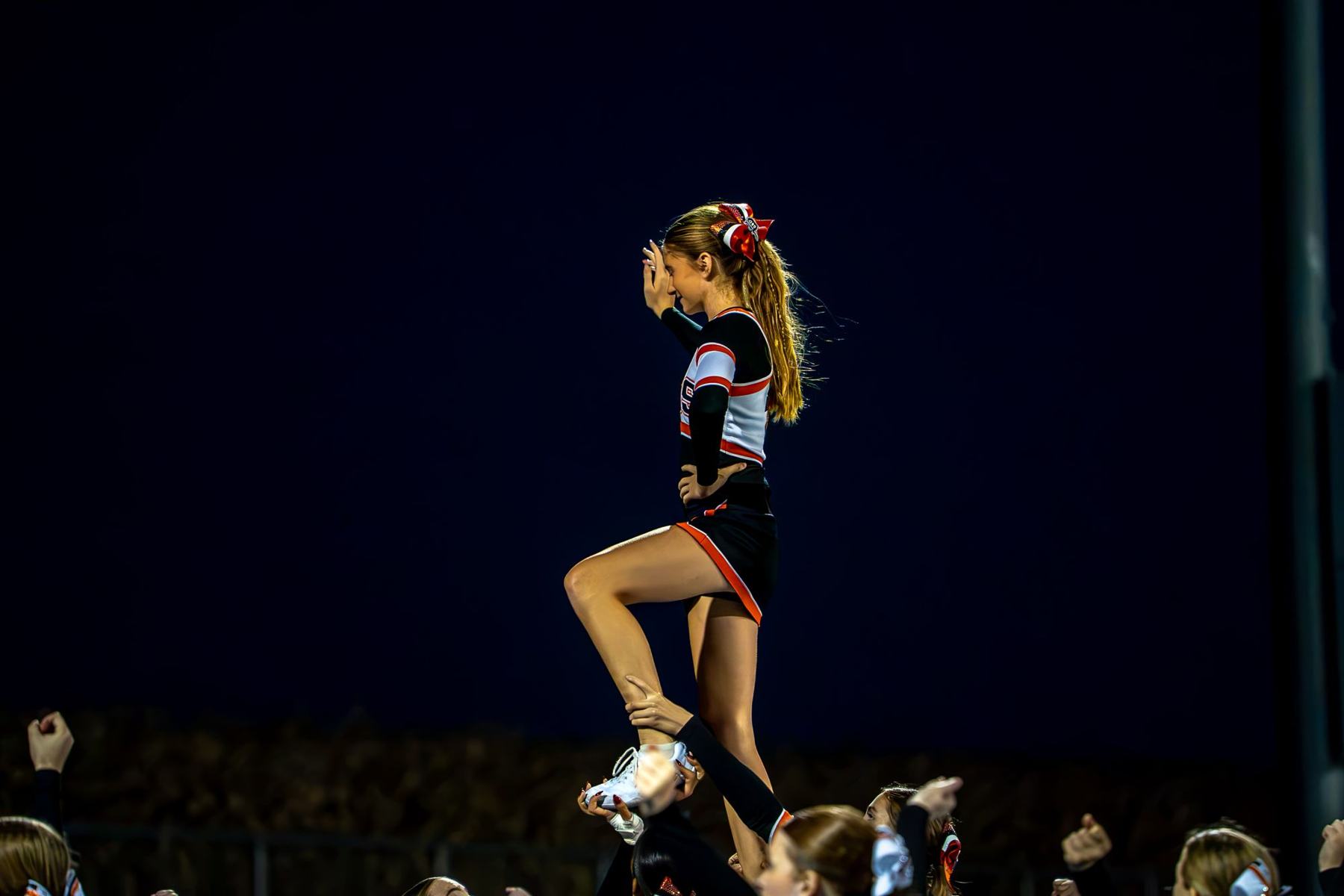 Cheerleader held mid-stunt against a dark night sky